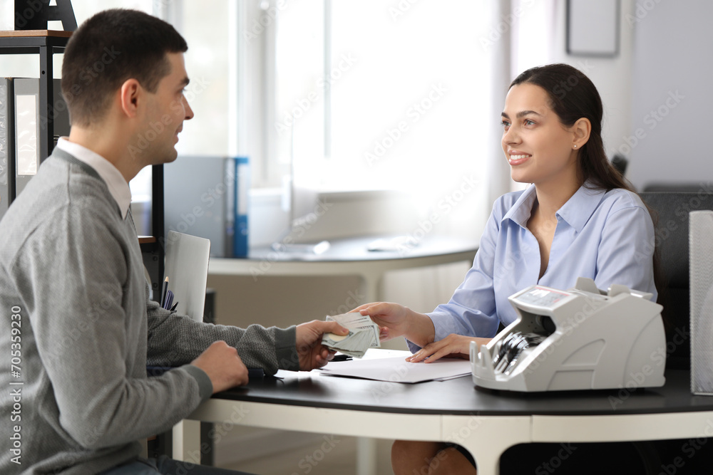 Young man giving money to bank manager in office Young man giving money to bank manager in office