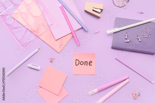 Sticky note with word DONE and stationery on lilac background