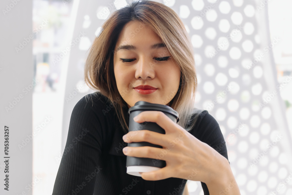 Happy Asian woman in black t-shirt sipping hot coffee in white coffee shop. Happy Asian woman in black t-shirt sipping hot coffee in white coffee shop.