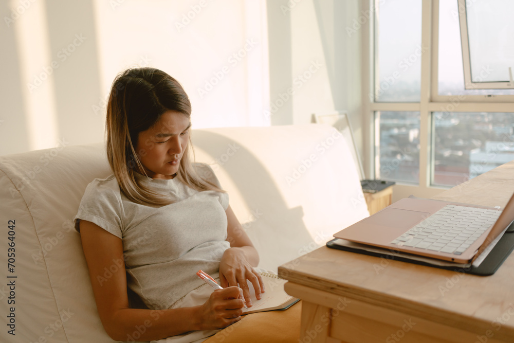 Asian woman taking note on paperworks with her pen in her apartment in concept of work from home. Asian woman taking note on paperworks with her pen in her apartment in concept of work from home.