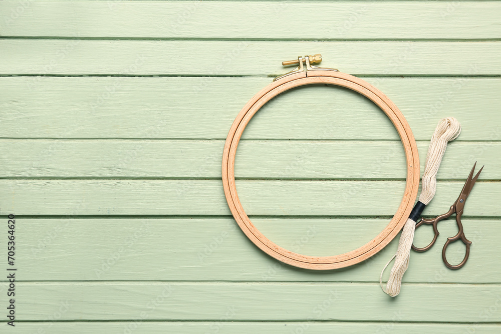 Wooden embroidery hoop with mouline thread and scissors on green wooden background Wooden embroidery hoop with mouline thread and scissors on green wooden background