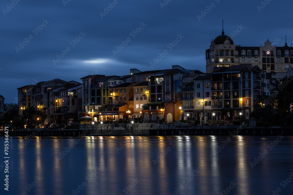 Buildings in a French architectural style photographed at night with lights and reflections of the lights in the water of a lake.