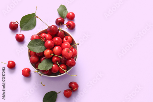 Tableau sur toile Bowl with sweet cherries and leaves on lilac background