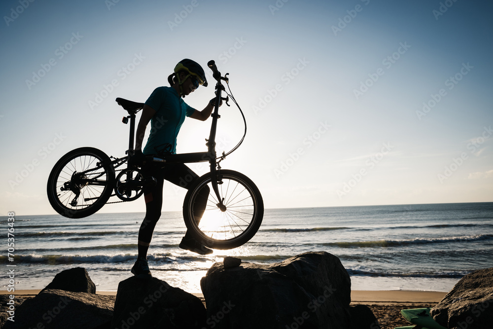 Fototapeta premium Woman taking a folding bike on sunrise seaside
