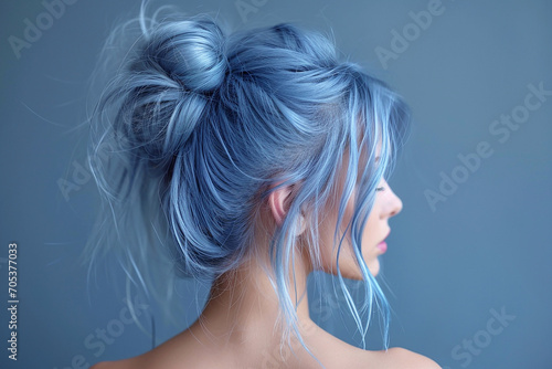 Profile of ayoung woman with blue hair with bun hairstyle on blue background close-up.