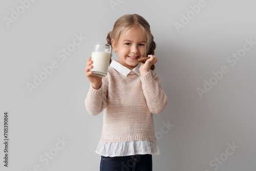 Cute little girl with glass of tasty milk and cookie on grey background