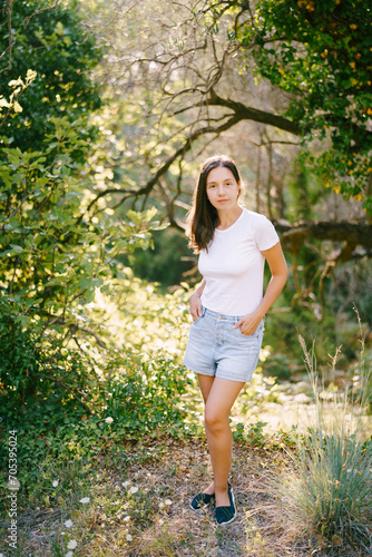 Young woman standing with hands in shorts pockets in green park