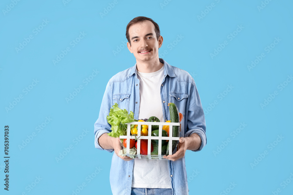 Young man with basket of fresh vegetables on blue background Young man with basket of fresh vegetables on blue background