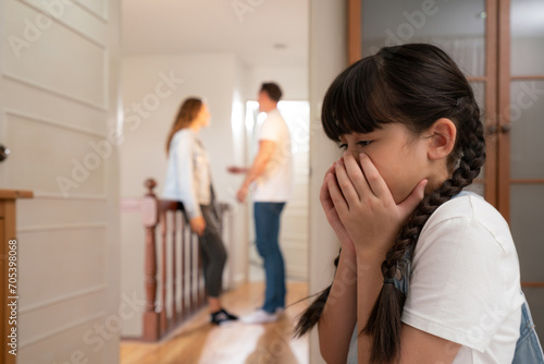 Stressed and unhappy young girl huddle in corner, cover her face while her parent arguing in background. Domestic violence at home and traumatic childhood develop to depression. Synchronos photo