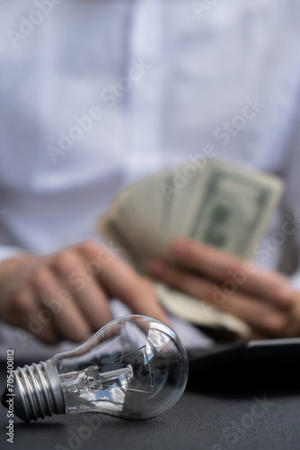 Electric light bulb. Man hands counting expenses bills on electricity banknotes of dollar cash accounting on calculator. Close up of hands unrecognizable Businessman. High prices for energy. Save up