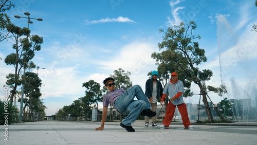 Asian skilled hipster doing freeze pose at camera surrounded by break dancer team near fountain with sky background. Group of handsome people practice b-boy dance. Outdoor sport 2024. Sprightly.