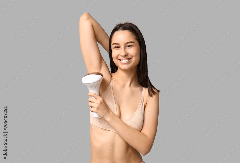 Happy young woman with modern photoepilator on grey background Happy young woman with modern photoepilator on grey background