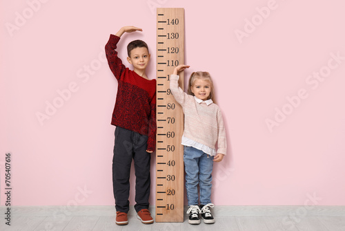 Cute little children measuring height near pink wall