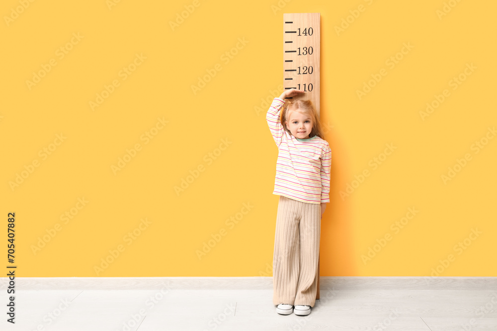 Cute little girl measuring height near yellow wall - obrazy, fototapety, plakaty 