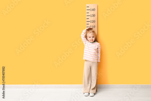 Cute little girl measuring height near yellow wall