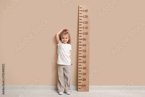 Cute little girl measuring height near beige wall photo