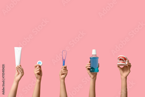 Female hands with supplies for oral hygiene and jaw model on pink background photo