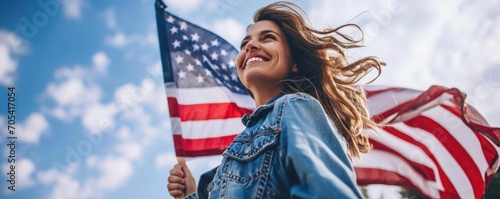 happy woman in denim jacket holding USA flag, smiling,standing against blue sky