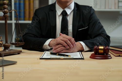 A lawyer sits with his hands on his desk reading the legal code on a clipboard, studying the constitution. Contract documents to protect human rights, judge working with law books, scales, hammer.