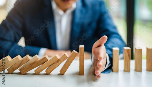Businessman halts falling domino with hand, symbolic of control and preventing chain reaction photo
