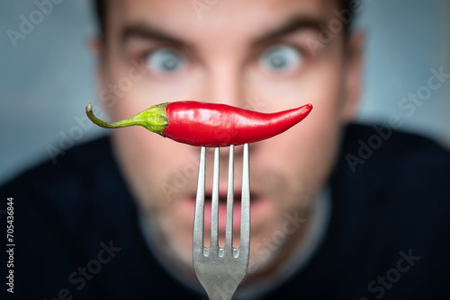 a man is afraid to eat hot peppers. ridiculous expression of a man with hot chillies in his hand
