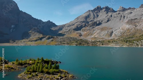 Aerial flyover over islands in the waters of Lac de Salanfe in Valais, Switzerland on a sunny autumn day in the Swiss Alps with a pan down view from peaks and cliffs to an overhead view of trees. photo