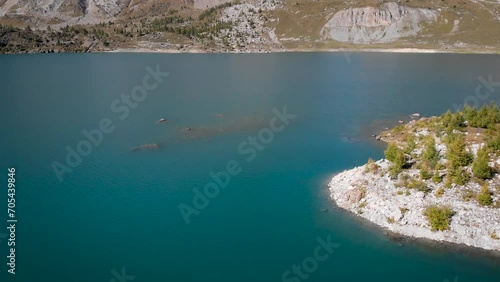 Aerial flyover over islands in the waters of Lac de Salanfe in Valais, Switzerland on a sunny autumn day in the Swiss Alps with a pan up view to surrounding alpine peaks and cliffs. photo