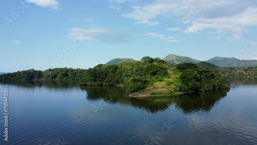 Aerial approaching shot of green vegetated Rainforest and lake with mountains in background during sunny day - Biosphere natural reserve of Los tuxtlas photo