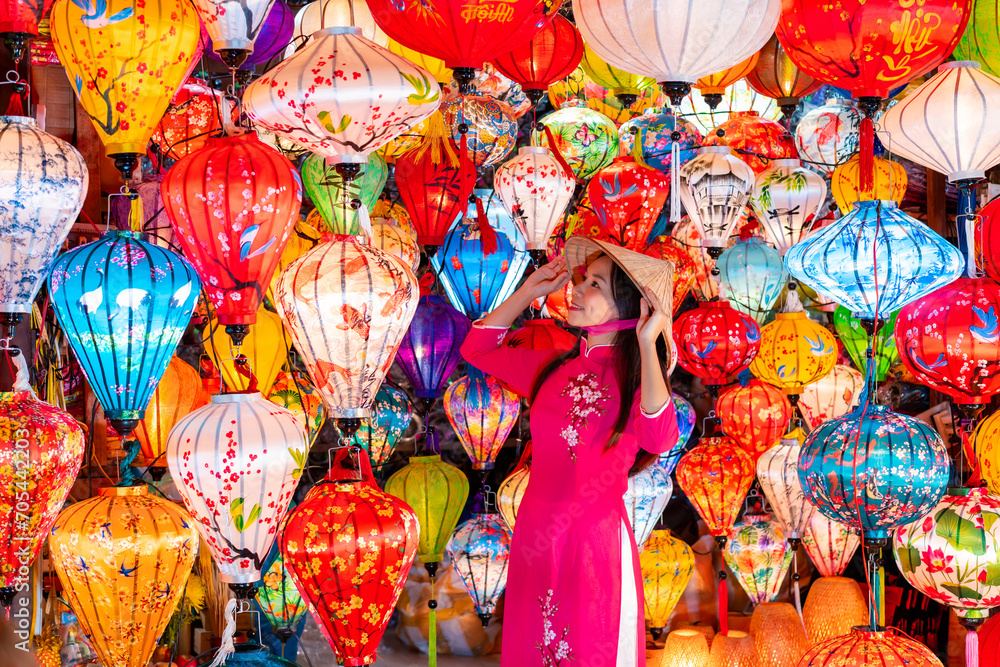 Young female tourist in Vietnamese traditional dress looking at Paper ornamental lanterns in Hoi An Ancient town