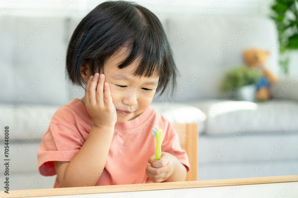 little asian girl presses hand to cheek, suffers from pain in tooth. Teeth decay, dental problems, child emotions and facial expression, oral health care, reducing sweets, fluorine coating. little asian girl presses hand to cheek, suffers from pain in tooth. Teeth decay, dental problems, child emotions and facial expression, oral health care, reducing sweets, fluorine coating.