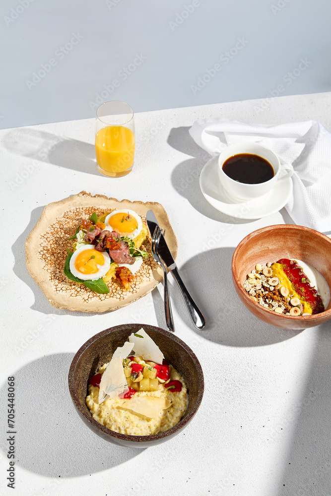 A complete breakfast set with sunny side up eggs, oatmeal, and yogurt with coffee and orange juice on a bright table