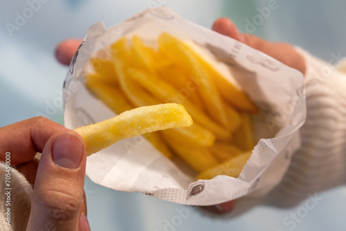 hand holds French fries in close-up. Eating junk food in a fast food cafe.