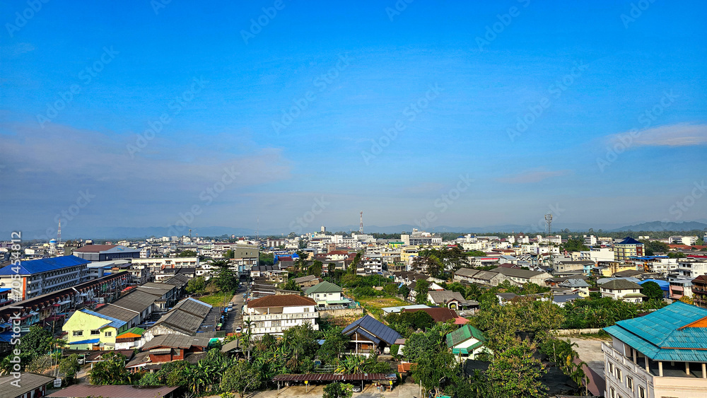 Fototapeta premium High angle shot view to the house-tops in Chumphon city is a southern of Thailand province city. Aerial view, Clear and bright day. city, landscape, village,building, school, sky, nature, clouds
