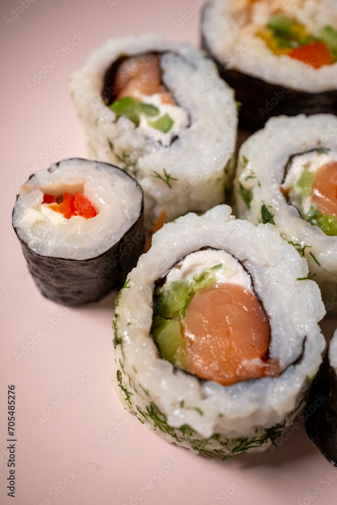 Chop sticks, mushrooms, noodle ramen, California rolls and Philadelphia rolls on a small plate on a pink background
