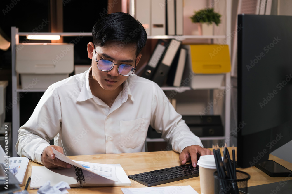 Fototapeta premium Young businessman working overtime on a desk at night..
