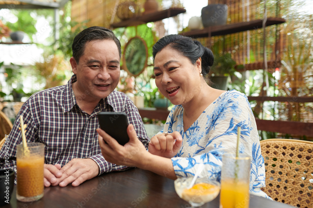 Excited senior woman showing photo on social media to husband