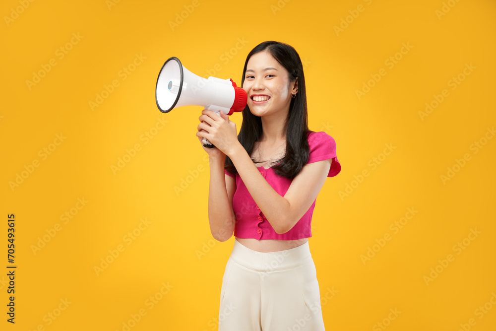 Portrait of a young Asian woman holding a megaphone in her hands and looking at the camera. Wearing a pink t-shirt and an isolated yellow background. Portrait of a young Asian woman holding a megaphone in her hands and looking at the camera. Wearing a pink t-shirt and an isolated yellow background.