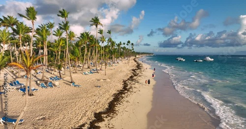 Tropical beach, caribbean sea and walking people on the sandy shore welcoming ocean sunrise over Punta Cana, Dominican Republic, aerial landscape photo