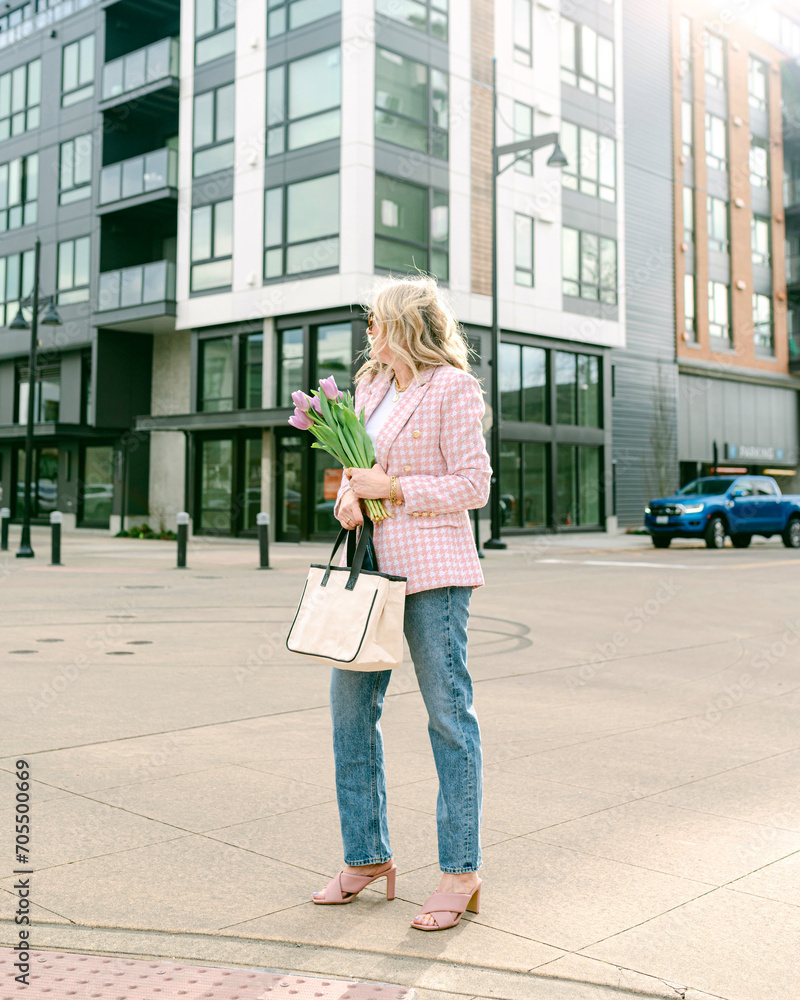 Stylish woman carrying tulips in the city on a spring day