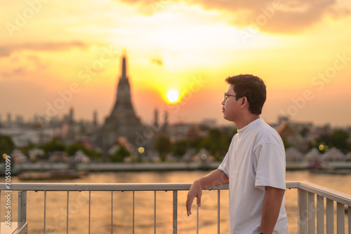 tourist man enjoys view to Wat Arun Temple in sunset, Traveler visits Temple of Dawn near Chao Phraya river from rooftop bar. Landmark and Travel destination in Bangkok, Thailand and Southeast Asia