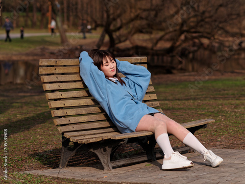 Beautiful young Chinese woman posing in sunny summer forest, wearing blue loose oversized top and miniskirt with small shoulder bag. Emotions, people, beauty, youth and lifestyle portrait.