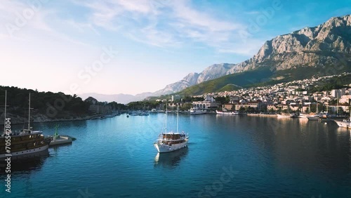 Zoom out shot of a majestic water body situated in valley amid the high mountain peaks with multiple small and large yachts and boats photo