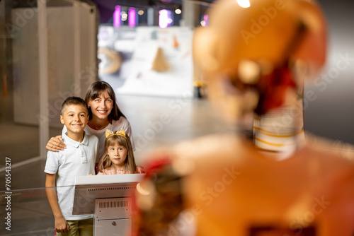 Фототапет Mom with kids are excited to interact with a robot, visiting together science museum