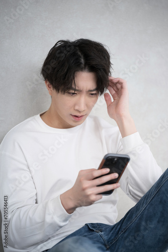 Handsome man holding a phone with a troubled or negative expression leaning against a wall.