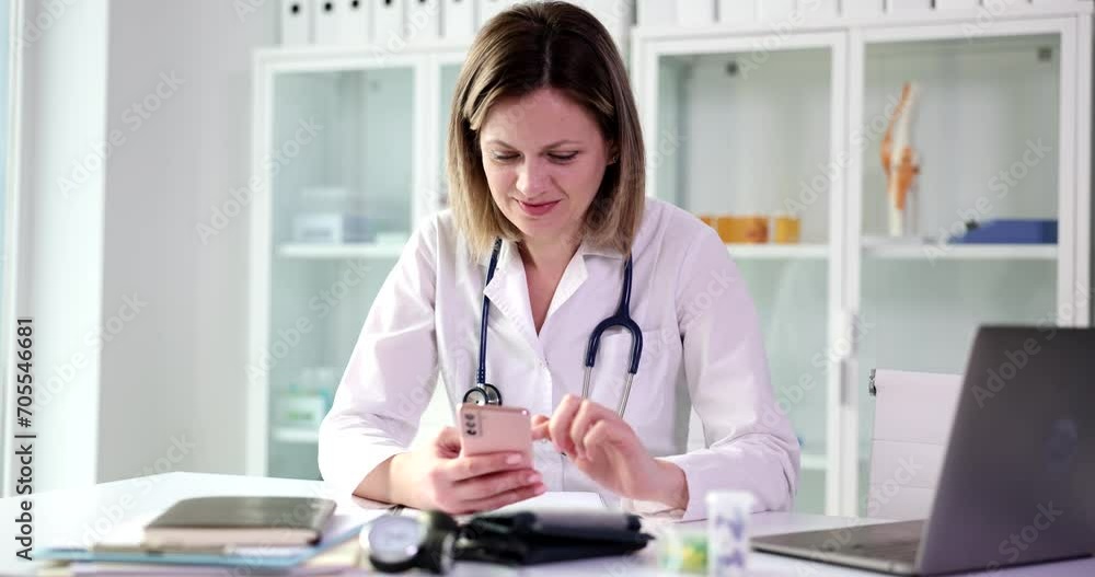 Beautiful therapist consults in clinic using smartphone application. Smiling female doctor holding mobile technology device sending text message and consulting remote patient online Beautiful therapist consults in clinic using smartphone application. Smiling female doctor holding mobile technology device sending text message and consulting remote patient online