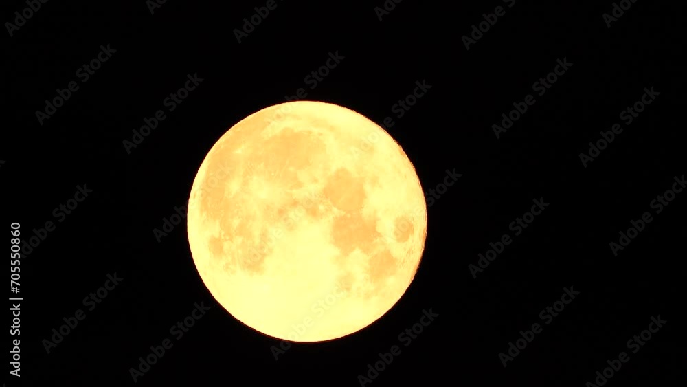 A glowing golden huge full moon seen from earth through the atmosphere against a starry night sky. A large full moon moves across the sky, the moon moving from the left frame to the right. A glowing golden huge full moon seen from earth through the atmosphere against a starry night sky. A large full moon moves across the sky, the moon moving from the left frame to the right.