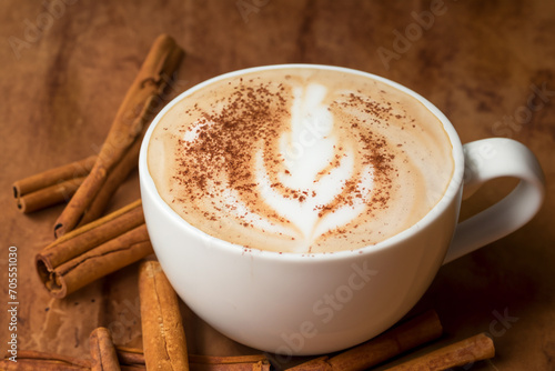 coffee composition. a cup of cappuccino with foam and a pattern of a tree leaf, cinnamon pods lie nearby, creative concept