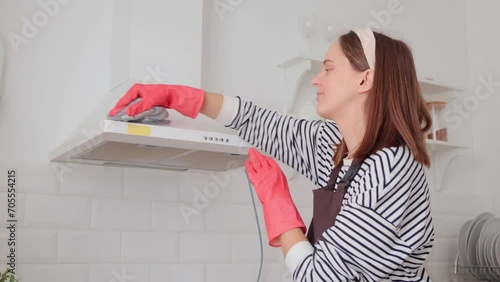 Caucasian brown haired woman cleaning kitchen hood with rag and detergent indoors doing her household chores housewife washing her house doing domestic routine photo