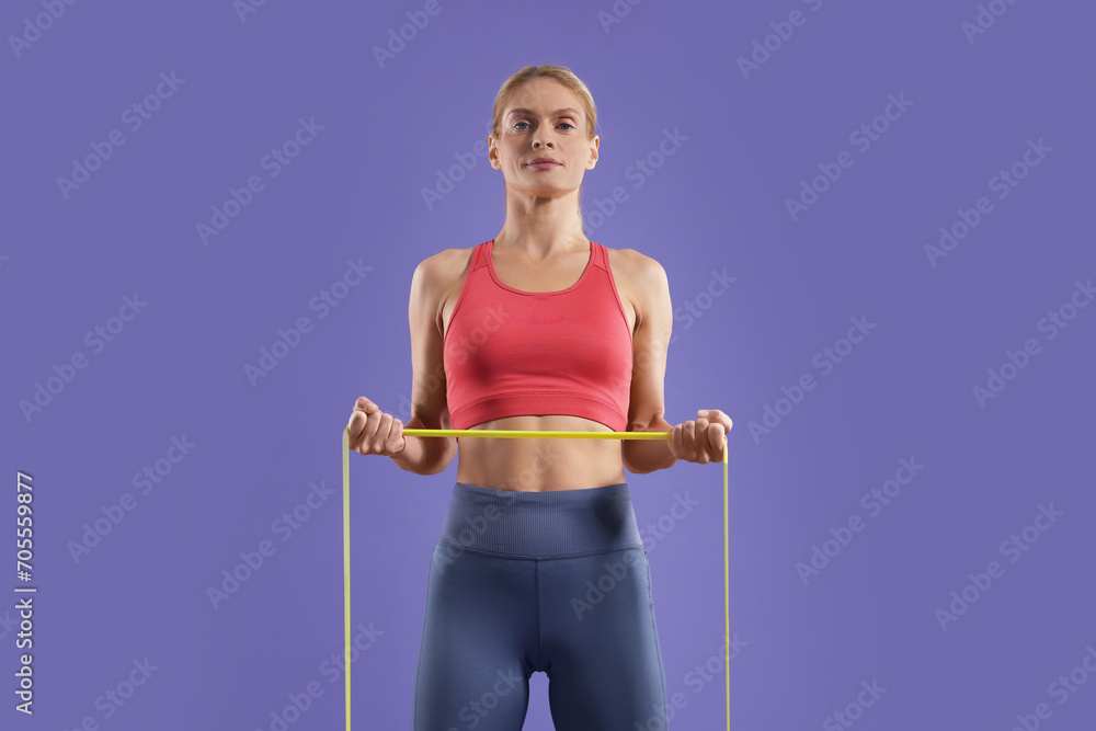 Athletic woman exercising with elastic resistance band on purple background, low angle view Athletic woman exercising with elastic resistance band on purple background, low angle view