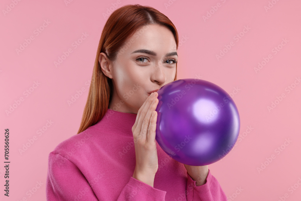 Woman inflating purple balloon on pink background Woman inflating purple balloon on pink background